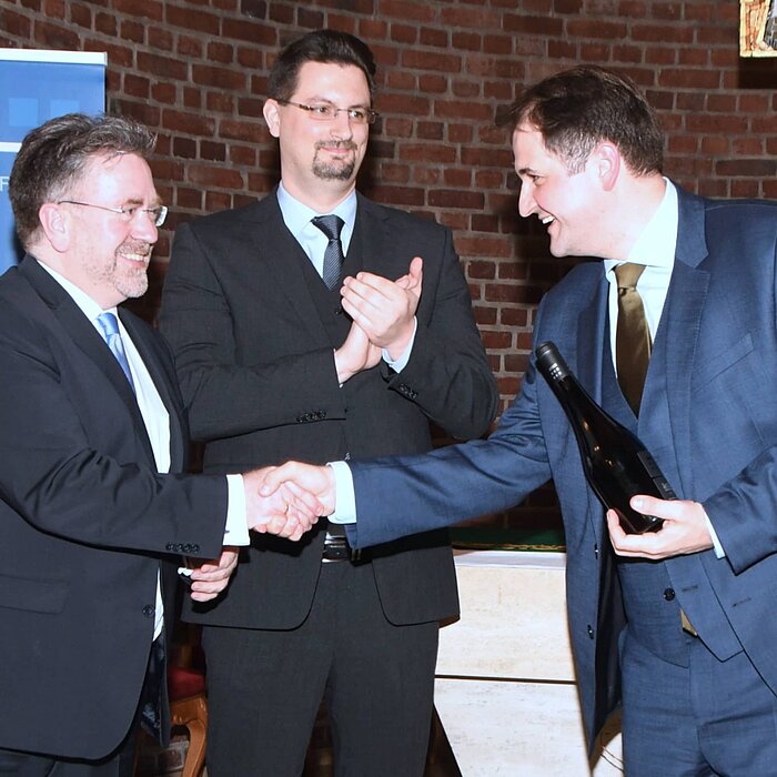 Das Bild zeigt Natanael Liminski, Christoph Konopka und Mathias Junggeburth. Während Christoph Konopka und Nathanael Liminski sich die Hände schütteln, klatscht Mathias Junggeburt würdigend in die Hände.