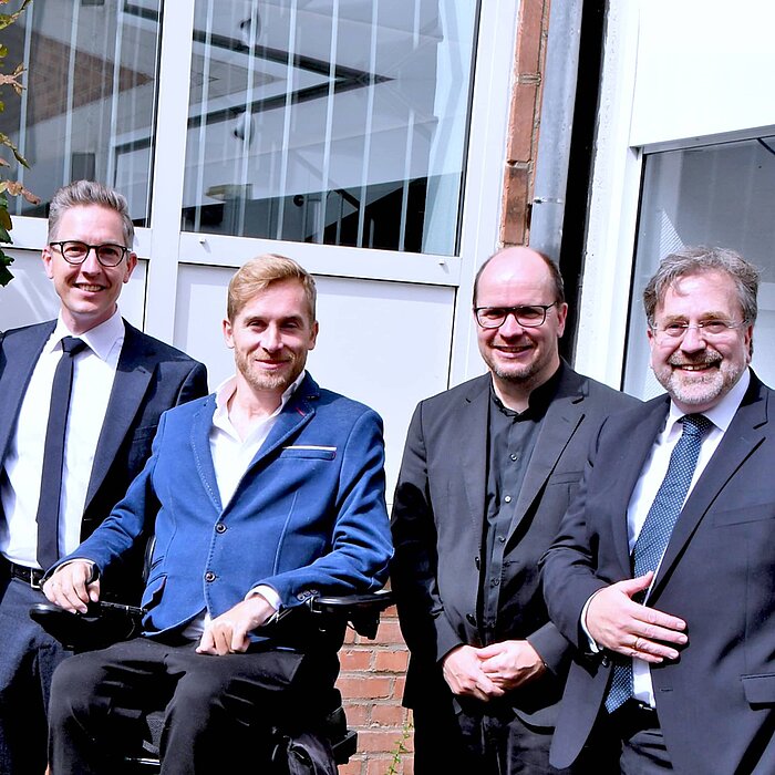 Man sieht ein Gruppenfoto mit Samuel Koch, Christoph Konopka, Pfarrer Dirk Bingener und Clemens Pollmann. Alle vier Personen tragen ein Jackett und lächeln in die Kamera. 